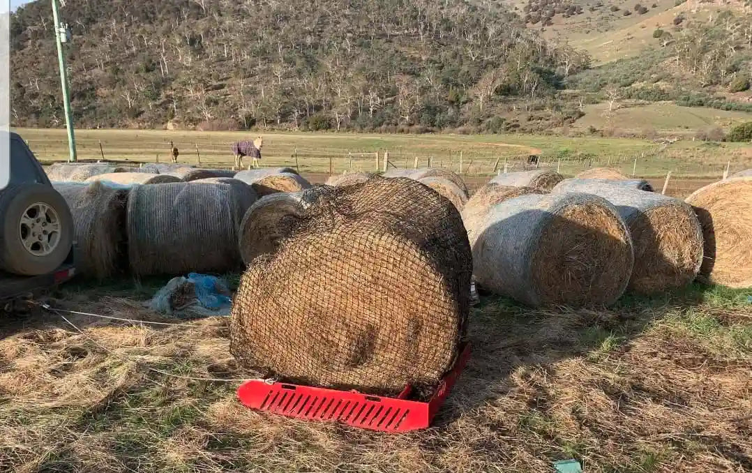 red paddock blade horse droppings collector carrying a round bale